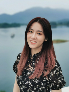 A woman stands smiling in front of a lake