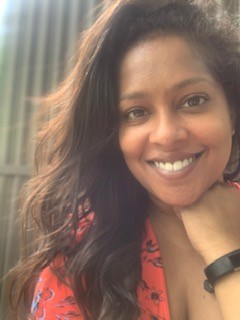 A woman in an orange shirt with brown hair smiles.