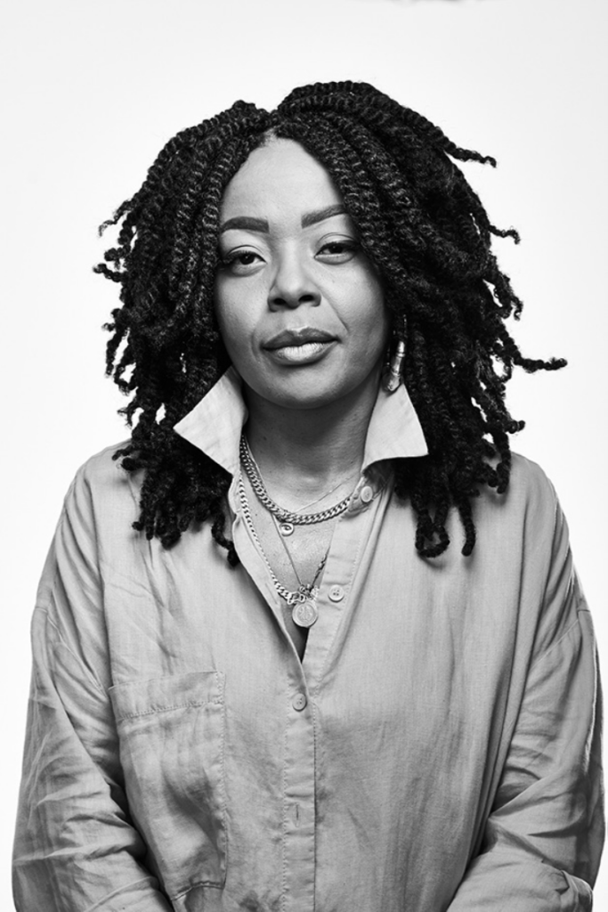 Headshot of Janelle Noel in black and white. She is wearing a button-up shirt with the collar popped, and several necklaces.